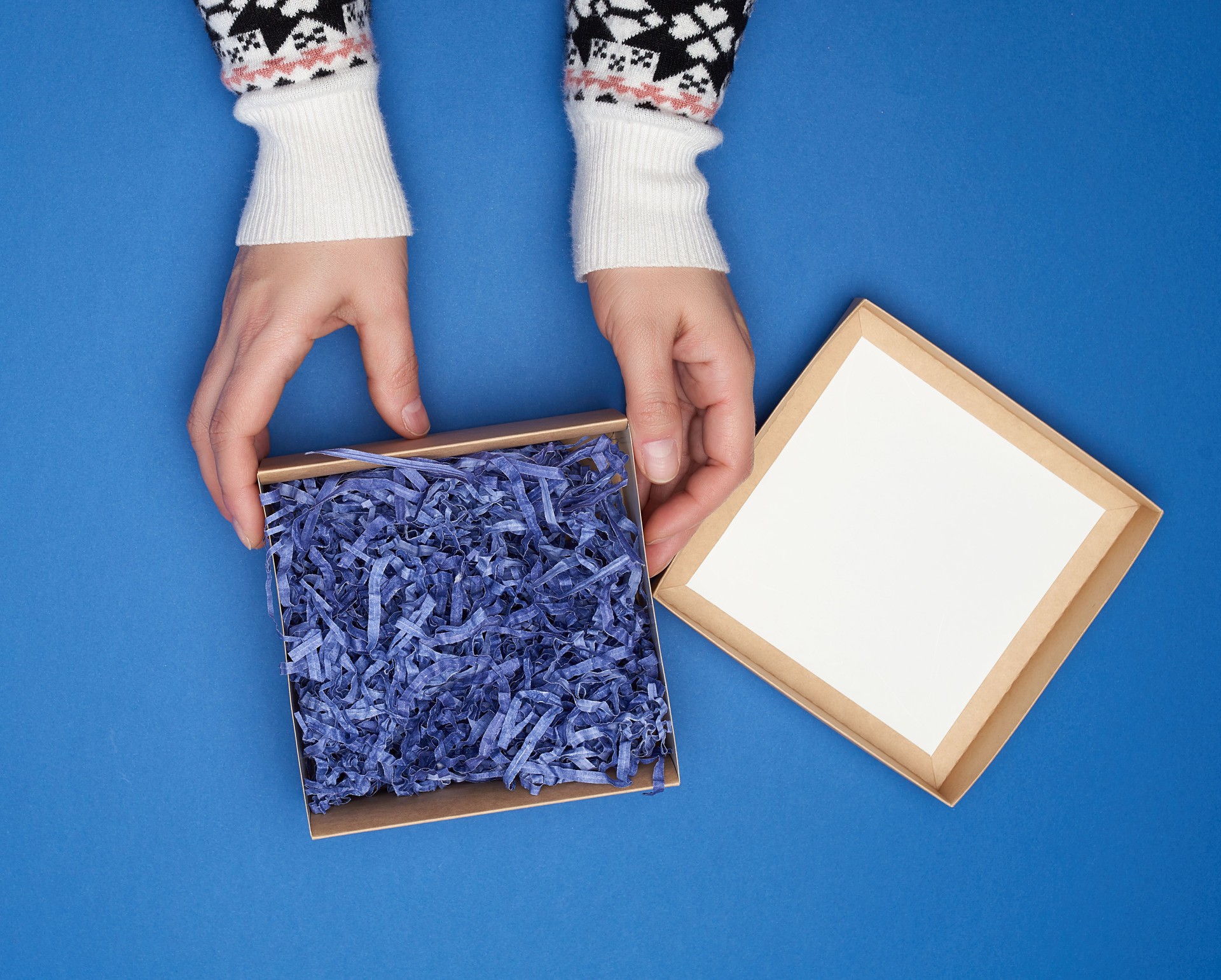 Cropped Hand Of Woman Holding Gift Box With Tinsel Over Blue Background